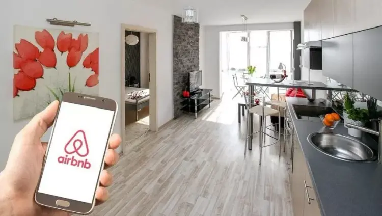 Hand holding a phone with the Airbnb app open in a rental apartment kitchen