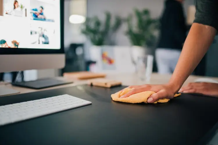 Wiping down an office desk near a computer monitor